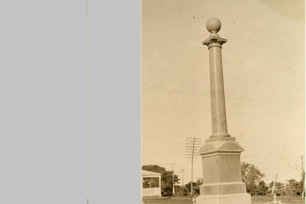 The Cenotaph stands at centre with a low chain fence and in background is the corner of the administration office and a slightly crooked power pole.