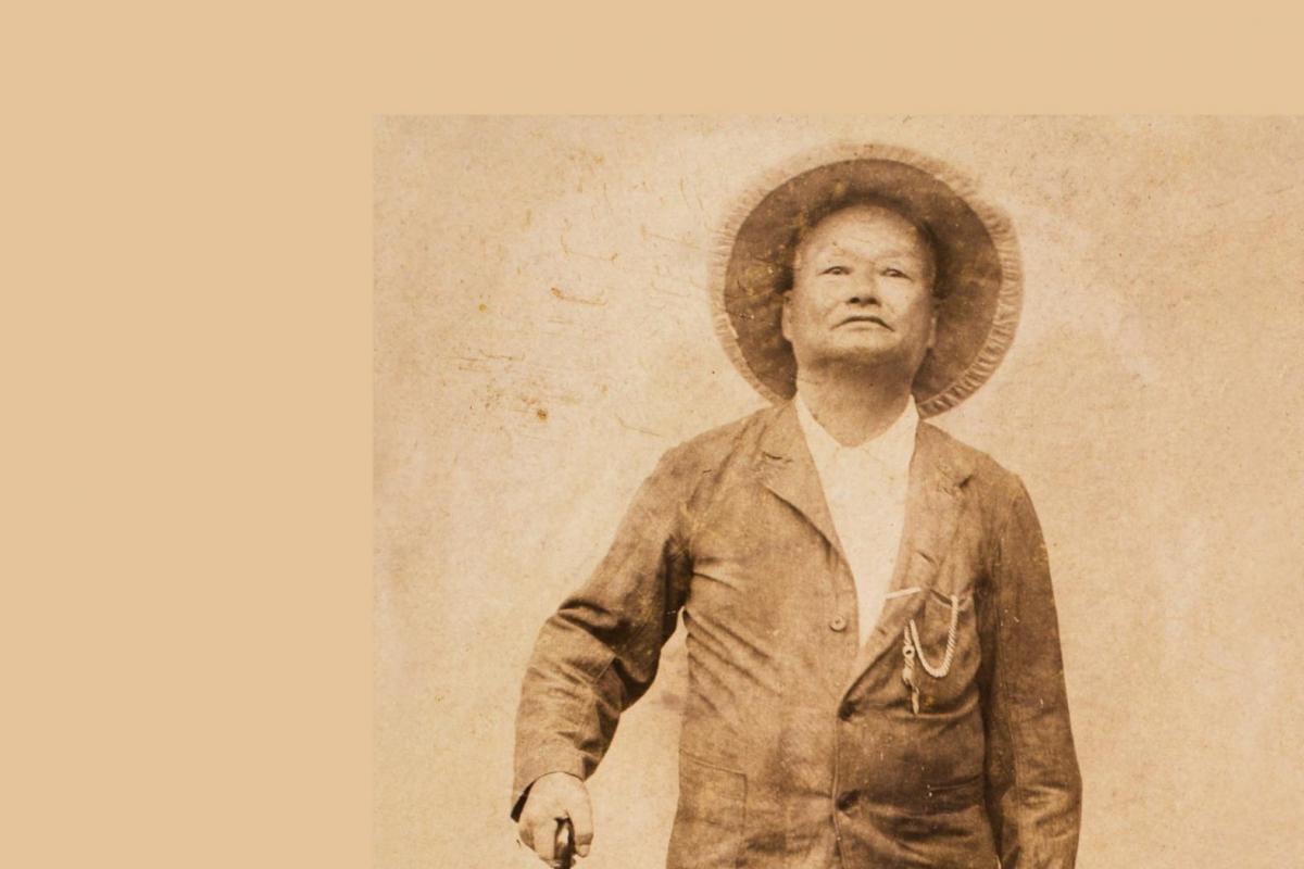 Man standing upright. He holds onto the handle of a folded umbrella by his side