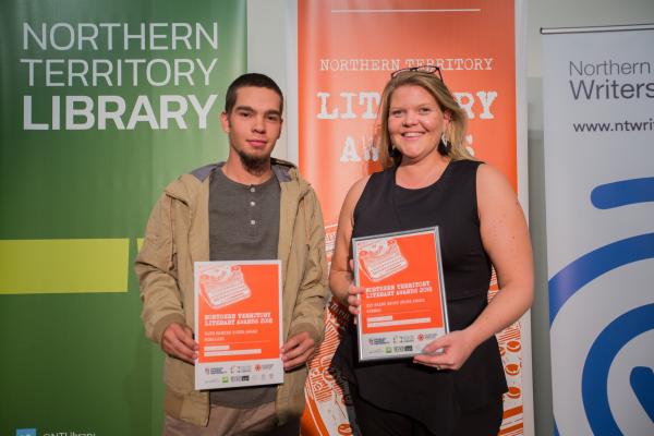 A young man and woman standing in front of banners holding certificates