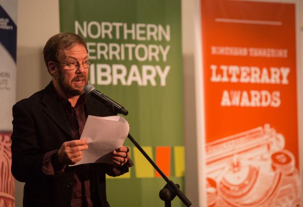 Man standing at microphone with banners positioned behind him 