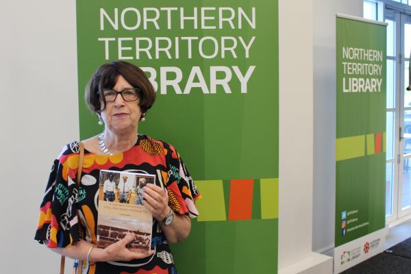 Woman standing in front of green signage, holding a book