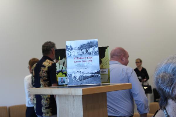 Book sitting on top of a book stand with people in conversation behind