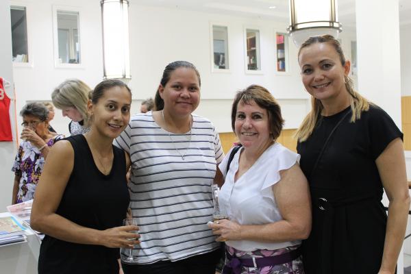 Four women standing in front of exhibition smiling at the camera