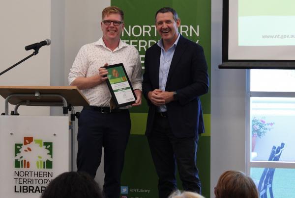 Two men standing and smiling, one receiving an Award
