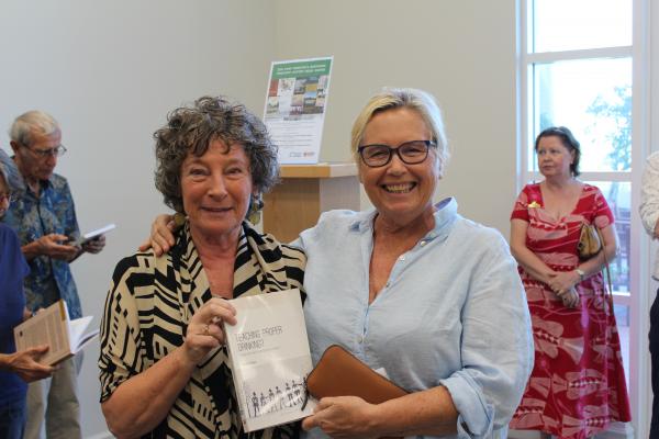 Two women smiling and holding onto a book