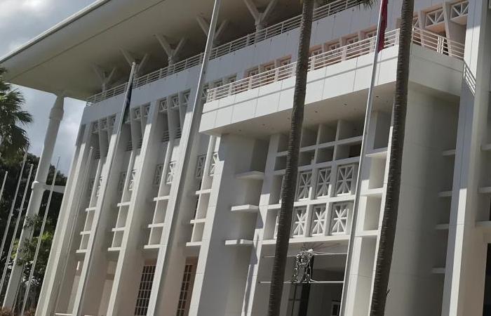Front of large white building with geometric patterns. Palm trees in foreground