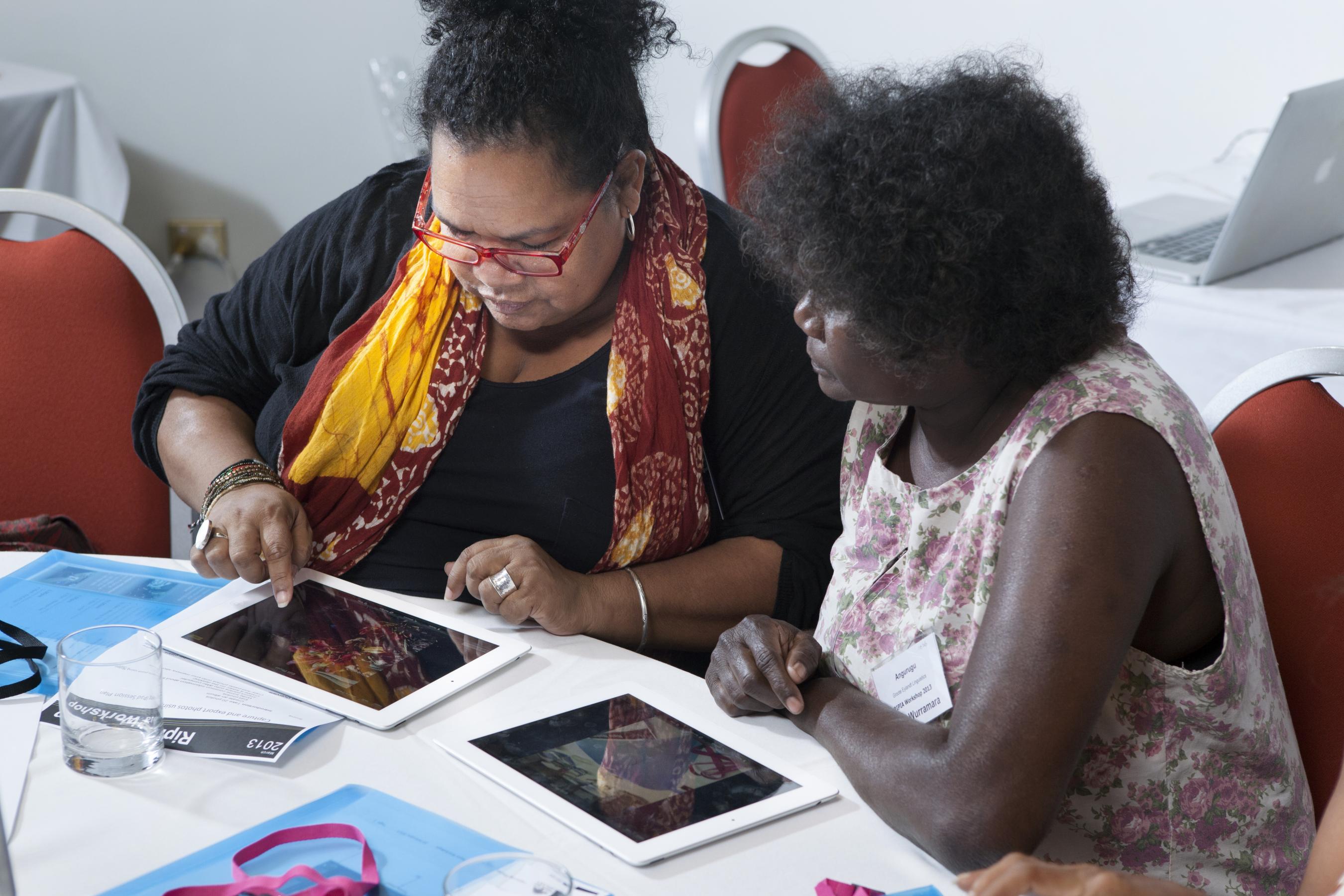 Two women sitting at a table using a tablet device
