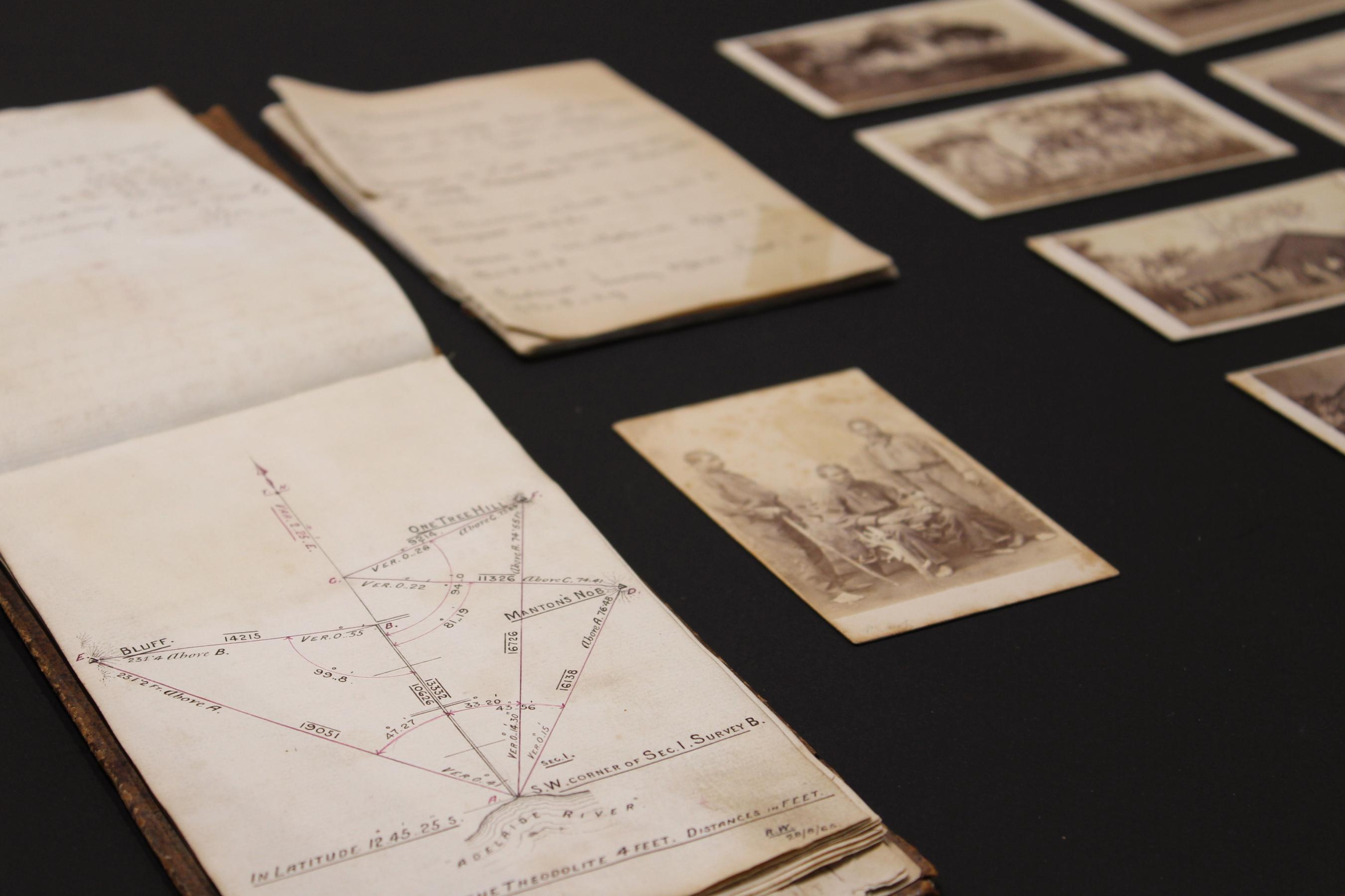 Notebooks and black and white photographs displayed on a black background.