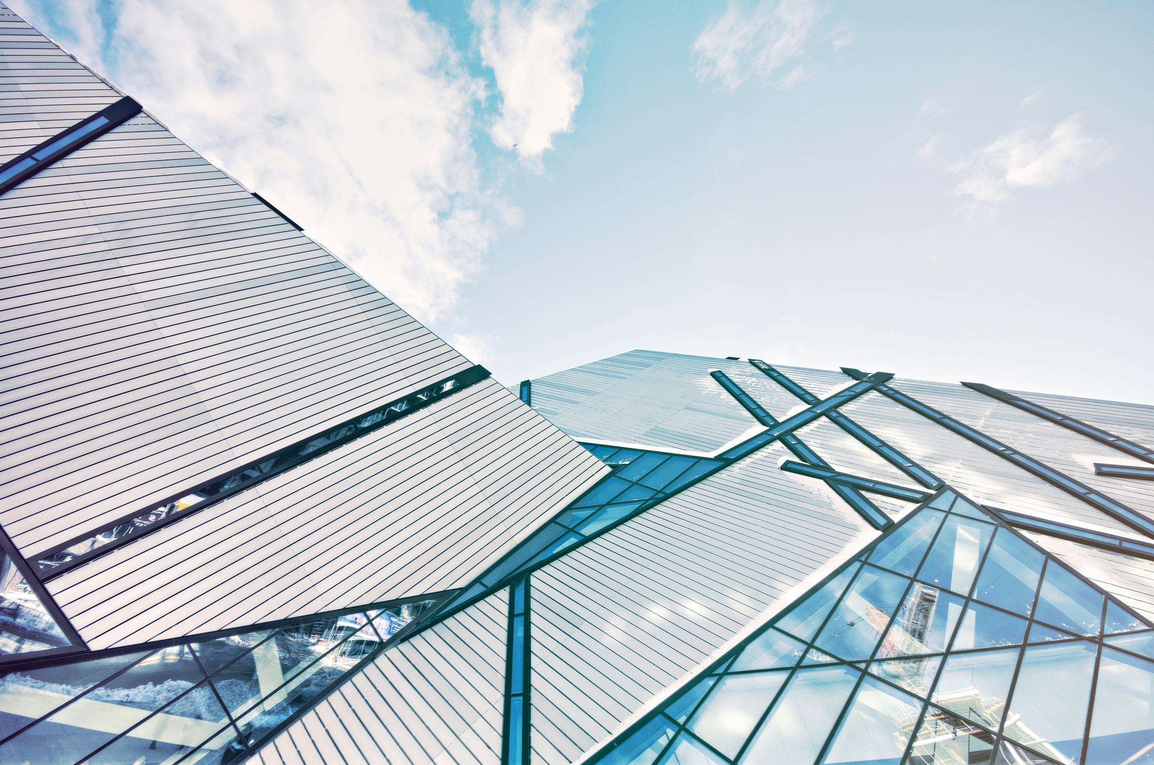 Looking up the side of a glass abstract building to blue sky above