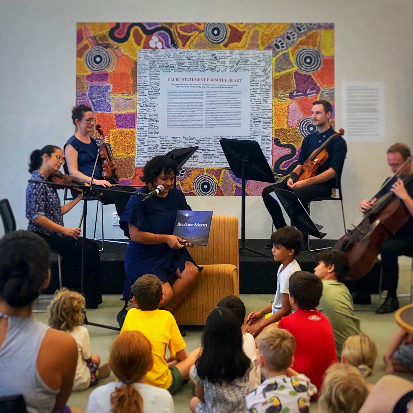 Reading a book, children listening, musicians playing.
