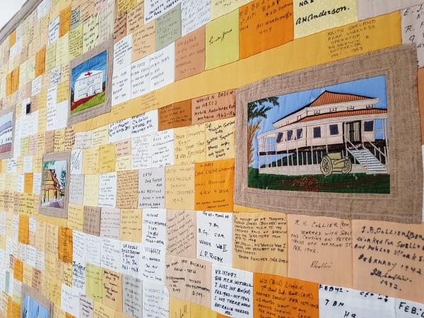Section of the Commemorative quilt. Photo is angled across the quilt revealing oranges toned patches with black writing on patches. Larger patches of iconic Darwin images scattered throughout names. 