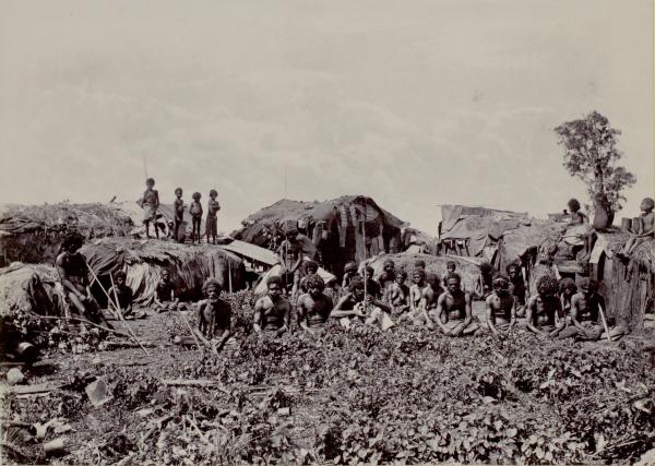 Depicts a group of Aboriginal men, women and children within a camp.